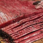 A partially sliced homemade pastrami on a wooden board.