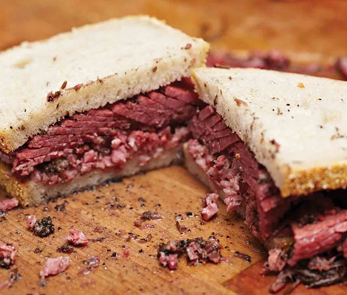 A pastrami sandwich mad with white bread and thinly sliced pastrami on a wooden cutting board.