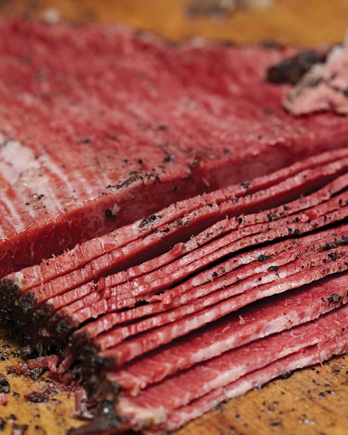 A partially sliced homemade pastrami on a wooden board.