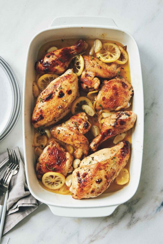A rectangular baking dish filled with roast chicken, lemon slices, and garlic cloves.