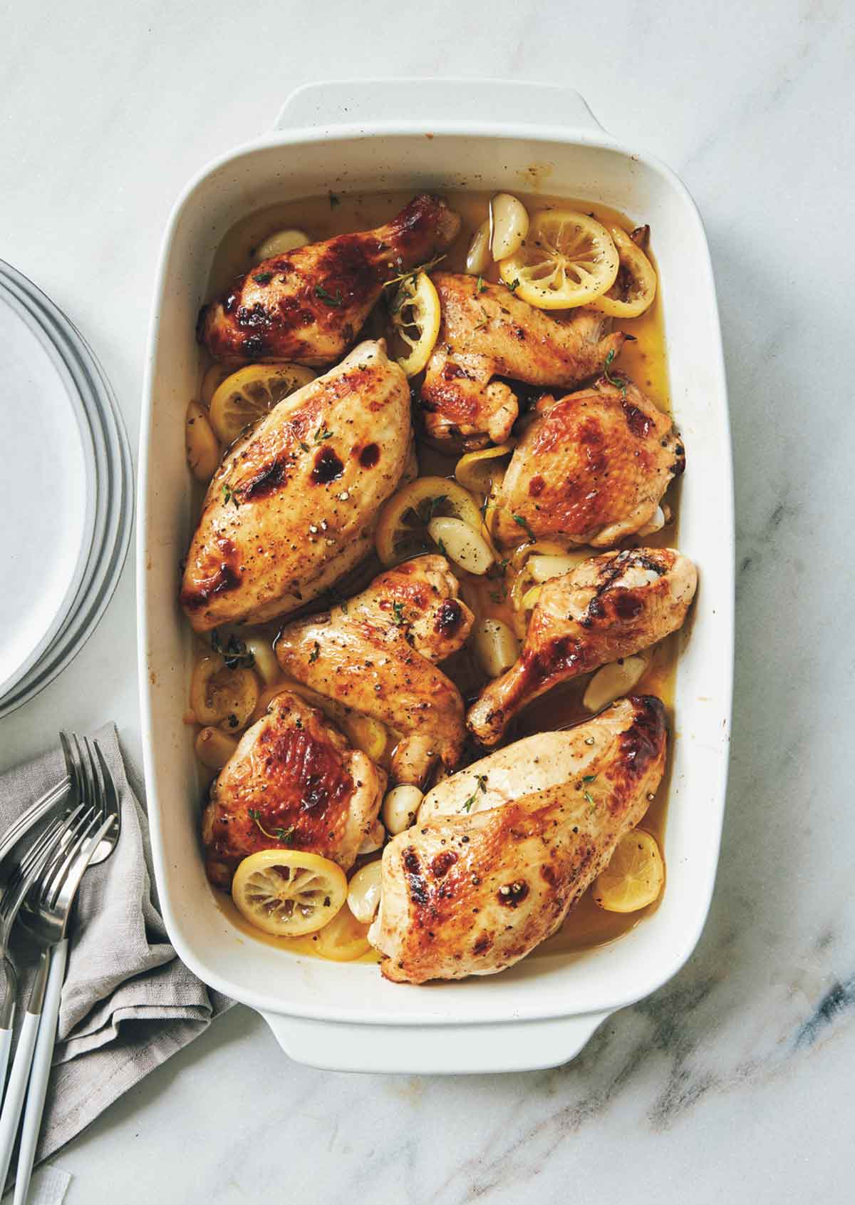 A rectangular baking dish filled with roast chicken, lemon slices, and garlic cloves.