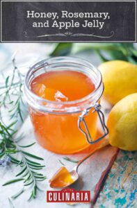 A jar of honey, rosemary, and apple jelly beside two lemons and a pile of rosemary twigs.