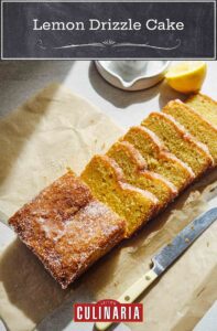 A loaf of lemon drizzle cake with six slices cut from it and a knife lying beside it.