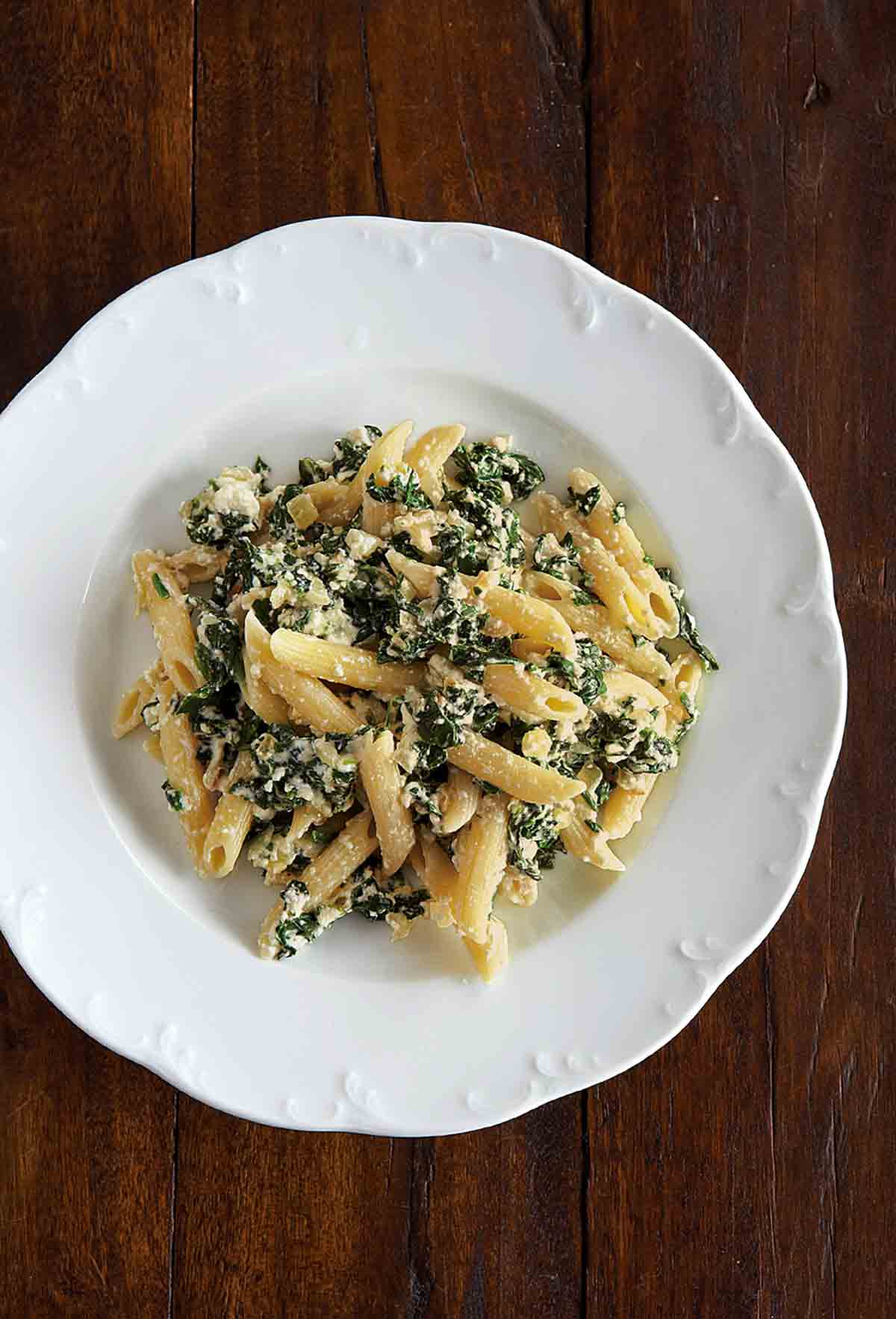 A white serving bowl filled with penne with spinach-ricotta sauce.