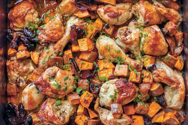 A sheet pan filled with roast chicken pieces, sweet potato chunks, dates, and a parsley garnish.