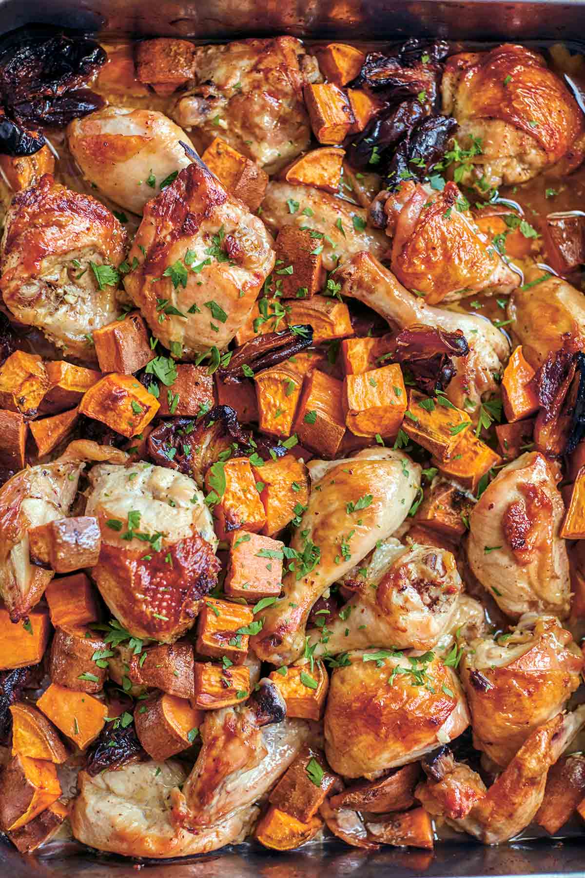 A sheet pan filled with roast chicken pieces, sweet potato chunks, dates, and a parsley garnish.