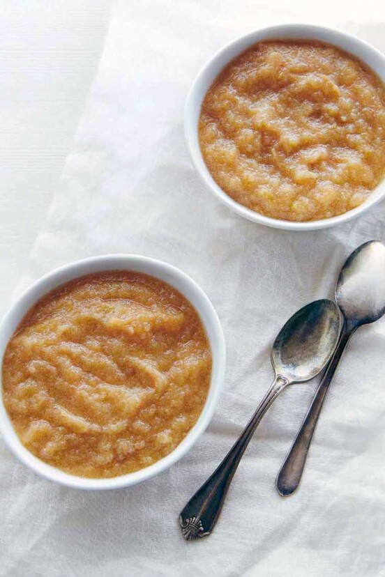 Two bowls of slow cooker applesauce with two spoons nearby.