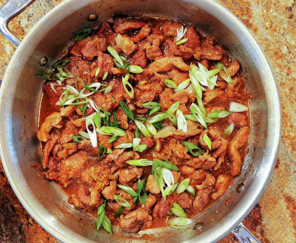 A stainless-steel skillet filled with Vietnamese caramelized pork, and topped with sliced scallions.