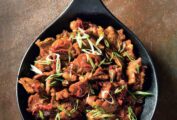 A cast-iron skillet filled with Vietnamese caramelized pork, and topped with sliced chiles and scallions.