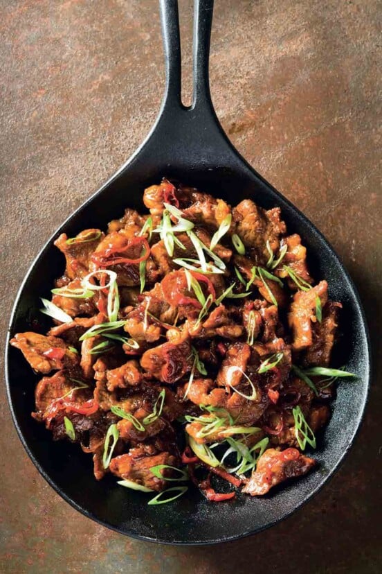 A cast-iron skillet filled with Vietnamese caramelized pork, and topped with sliced chiles and scallions.