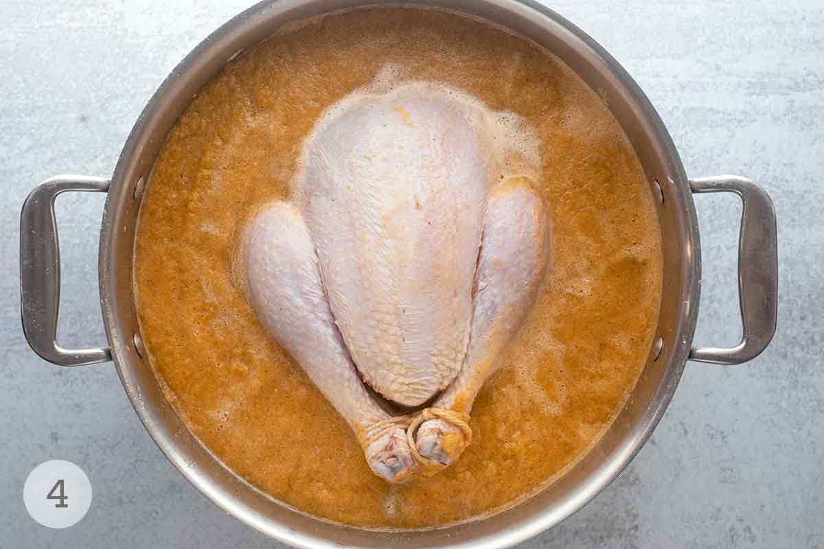 A whole chicken submerged in a pot of vegetable infused brine.