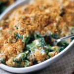 A white gratin dish filled with cheesy broccoli and topped with toasted breadcrumbs.