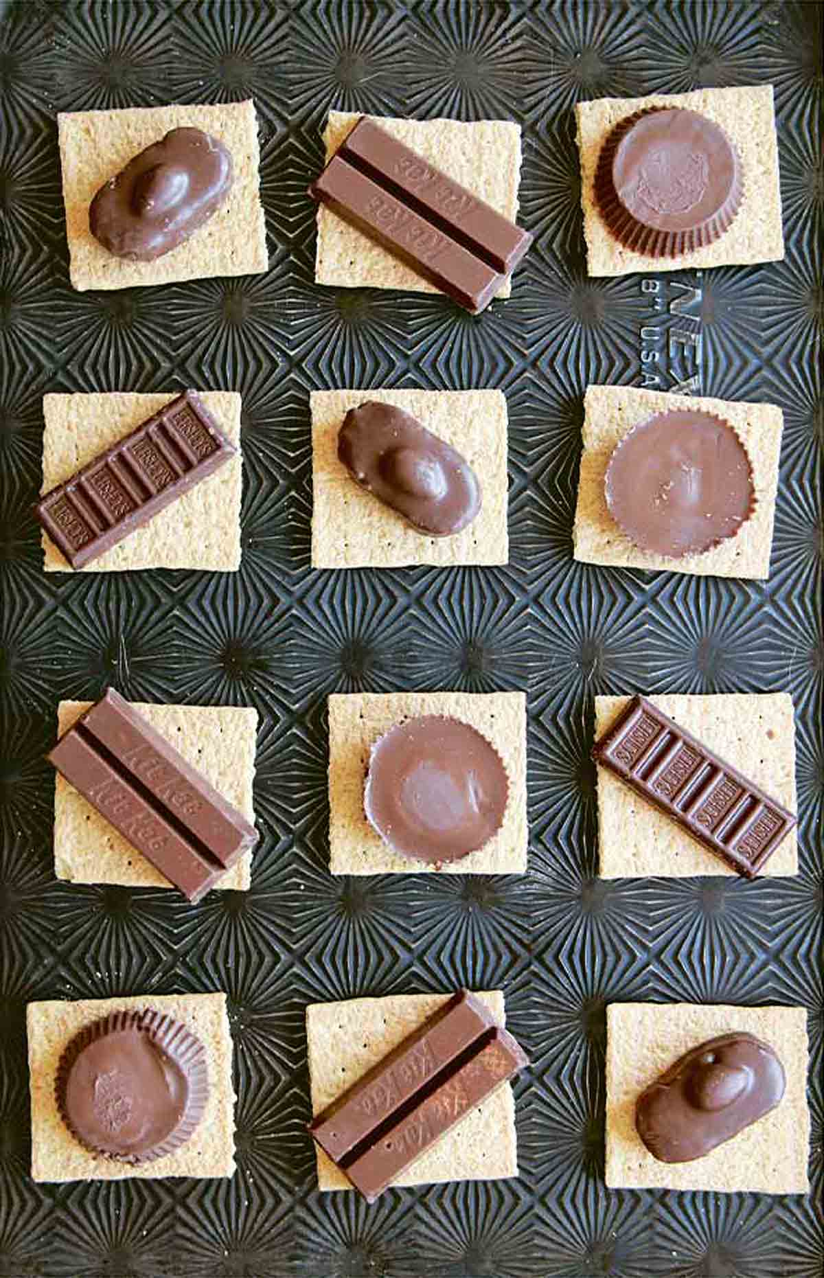 12 graham cracker squares topped with various candy bar pieces.