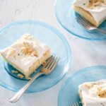 Three pieces of white cake topped with frosting and toasted coconut on individual blue glass plates with forks resting on the side.
