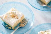 Three pieces of white cake topped with frosting and toasted coconut on individual blue glass plates with forks resting on the side.