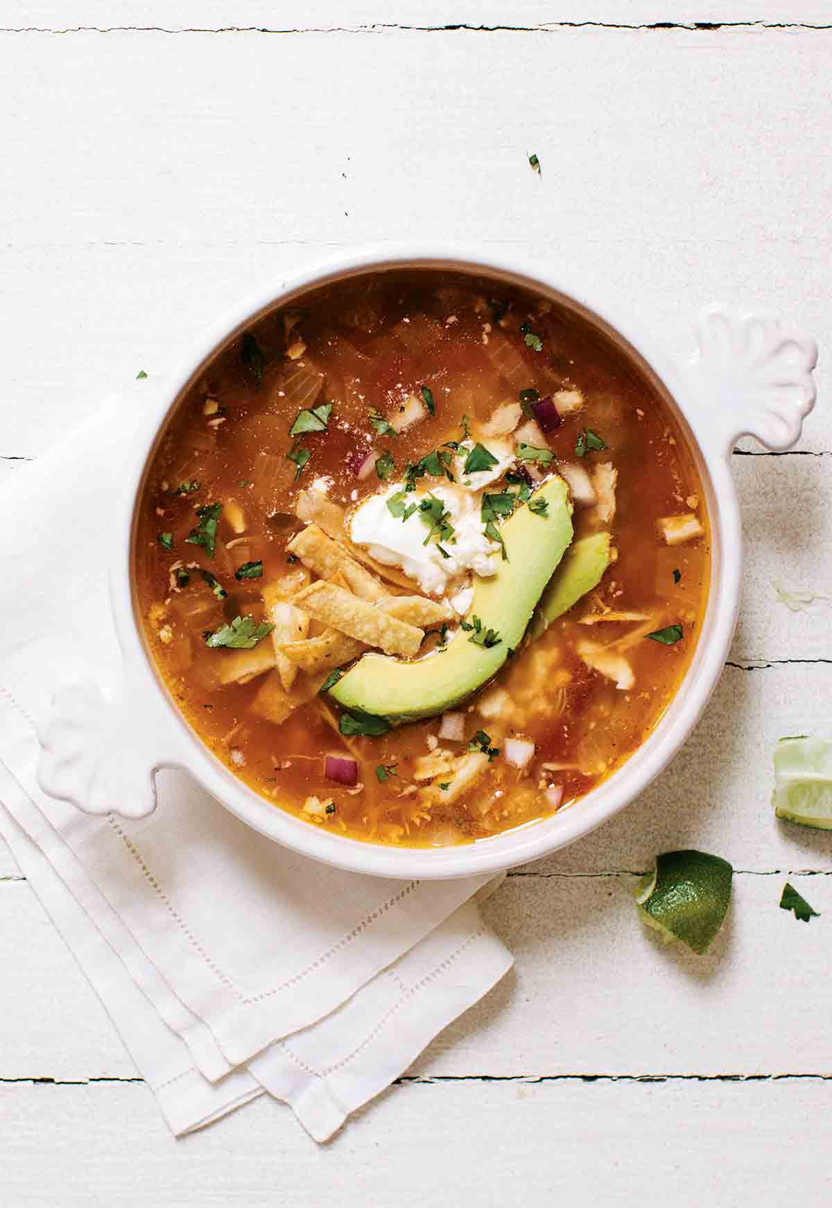 A bowl of easy chicken tortilla soup, with chicken, avocado, tortilla strips, and sour cream.