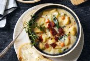 Two bowls of gnocchi soup, garnished with bacon and rosemary, with crusty bread on the side.