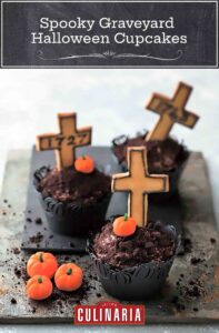 Three graveyard Halloween cupcakes with mini pumpkin candies and crosses on a piece of slate.
