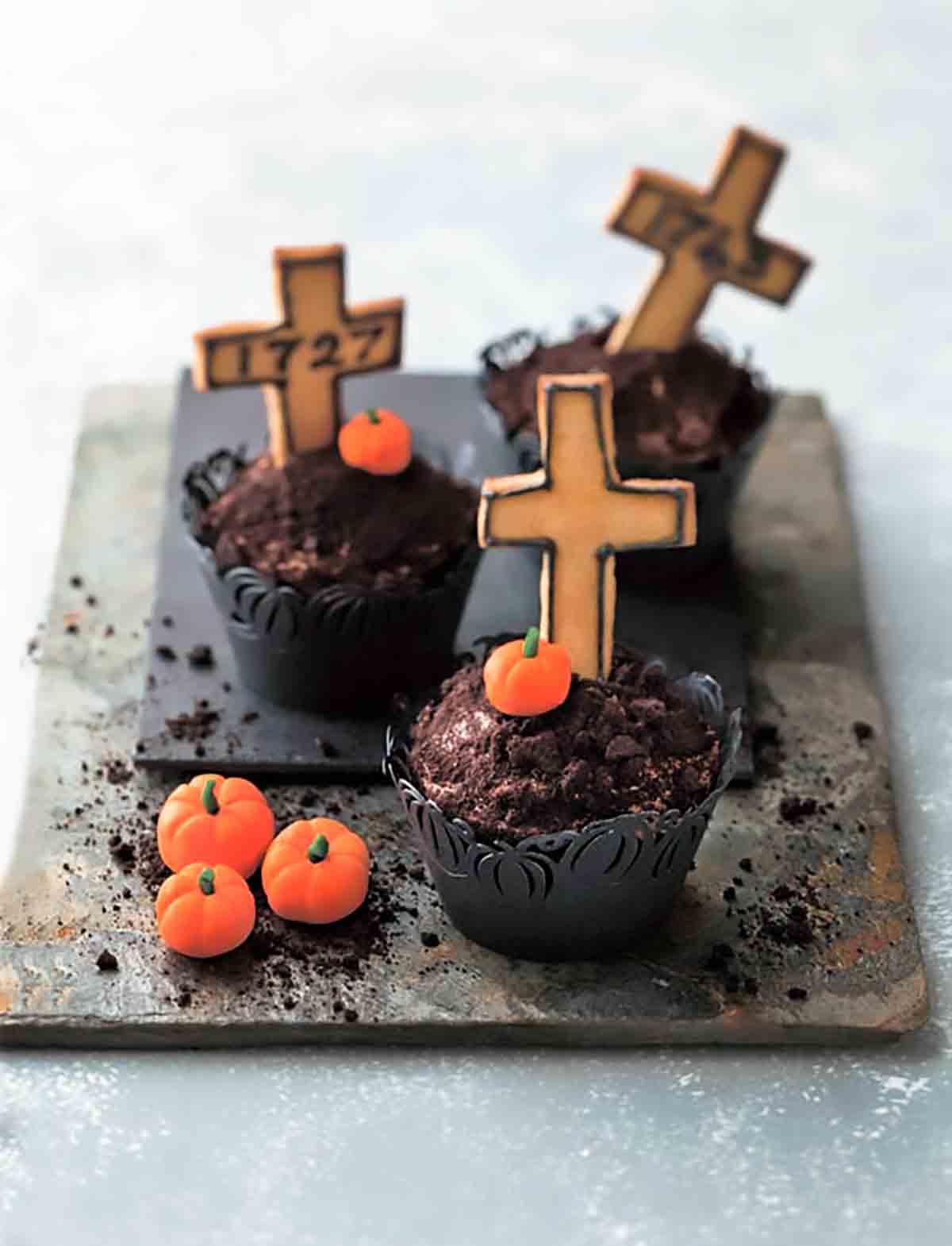 Tre kyrkogård Halloween cupcakes med mini pumpa godis och kors på en bit av skiffer.