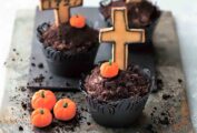 Three graveyard Halloween cupcakes with mini pumpkin candies and crosses on a piece of slate.