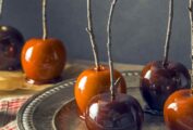 Caramel apples with branch sticks sitting on a metal dish, with more in the background.