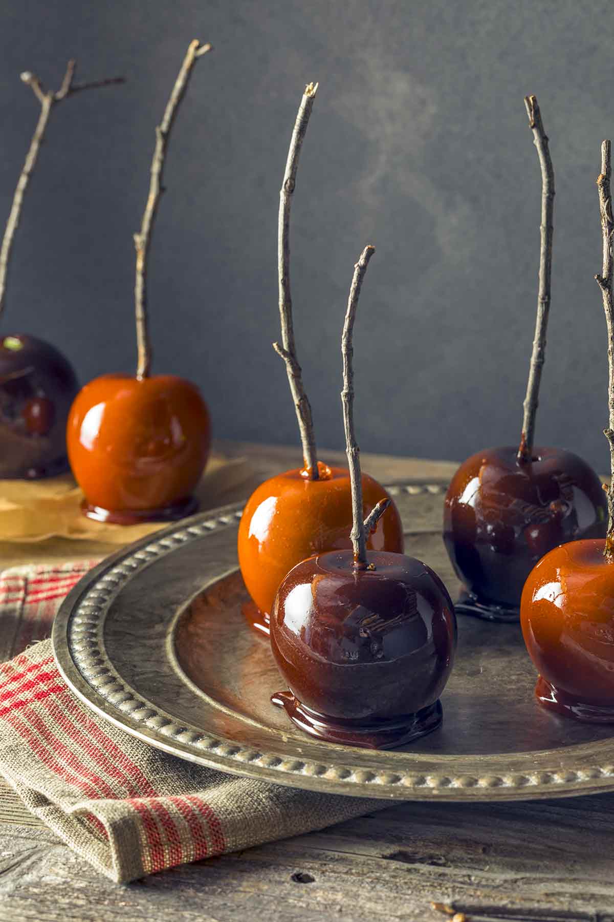 Caramel apples with branch sticks sitting on a metal dish, with more in the background.