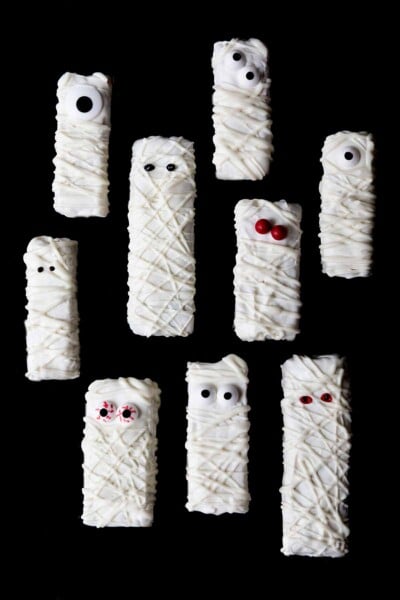 Nine Halloween mummy Rice Krispies treats with googly candy eyes on a black background.