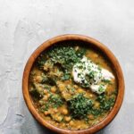 A wooden bowl filled with lentil soup with kale, topped with parsley and sour cream.