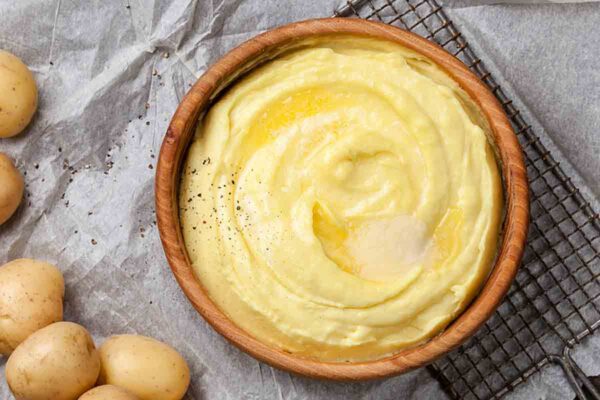 A wooden bowl filled with mashed potatoes and topped with a melted square of butter.