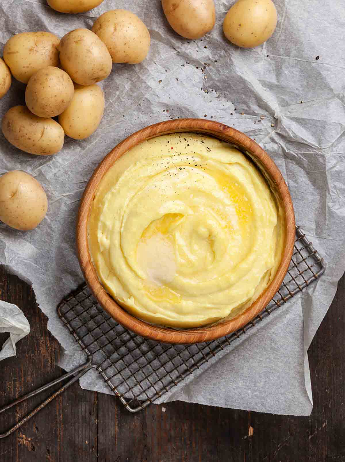 A wooden bowl filled with mashed potatoes and topped with a melted square of butter.