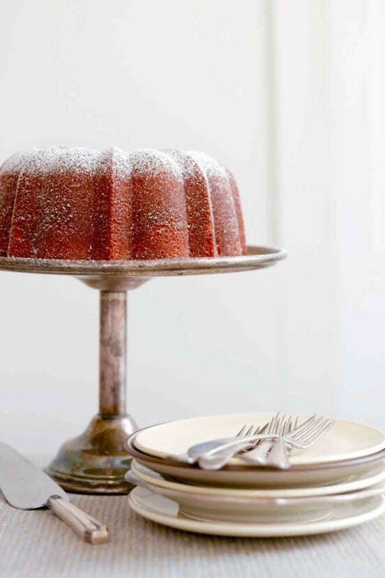 A Portuguese orange olive oil cake, dusted with confectioners' sugar on a silver cake stand.