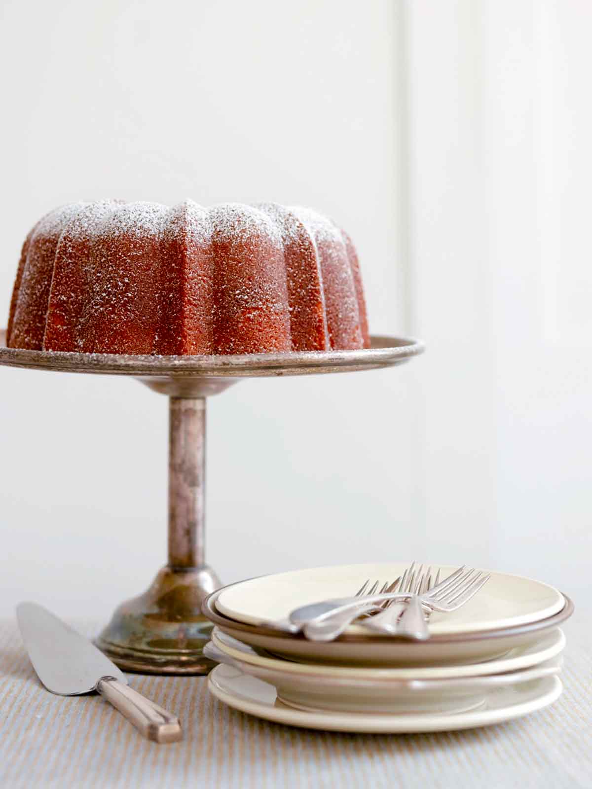A Portuguese orange olive oil cake, dusted with confectioners' sugar on a silver cake stand.