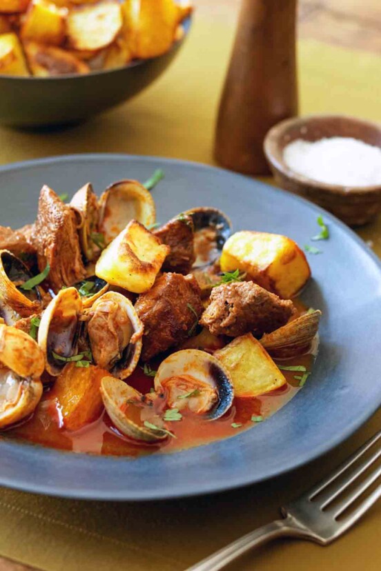 A blue bowl filled with Portuguese pork with clams and fried potato cubes.