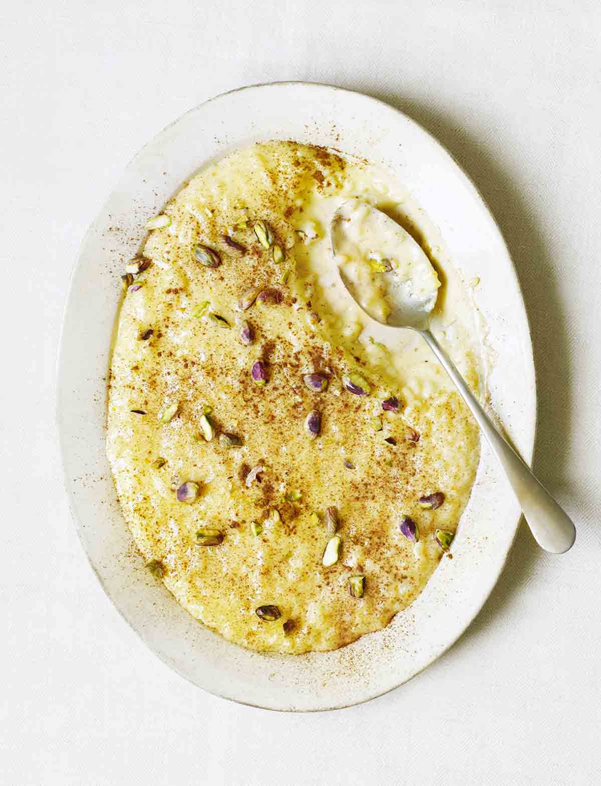 A white serving platter filled with Portuguese rice pudding and topped with toasted pistachios and cinnamon.