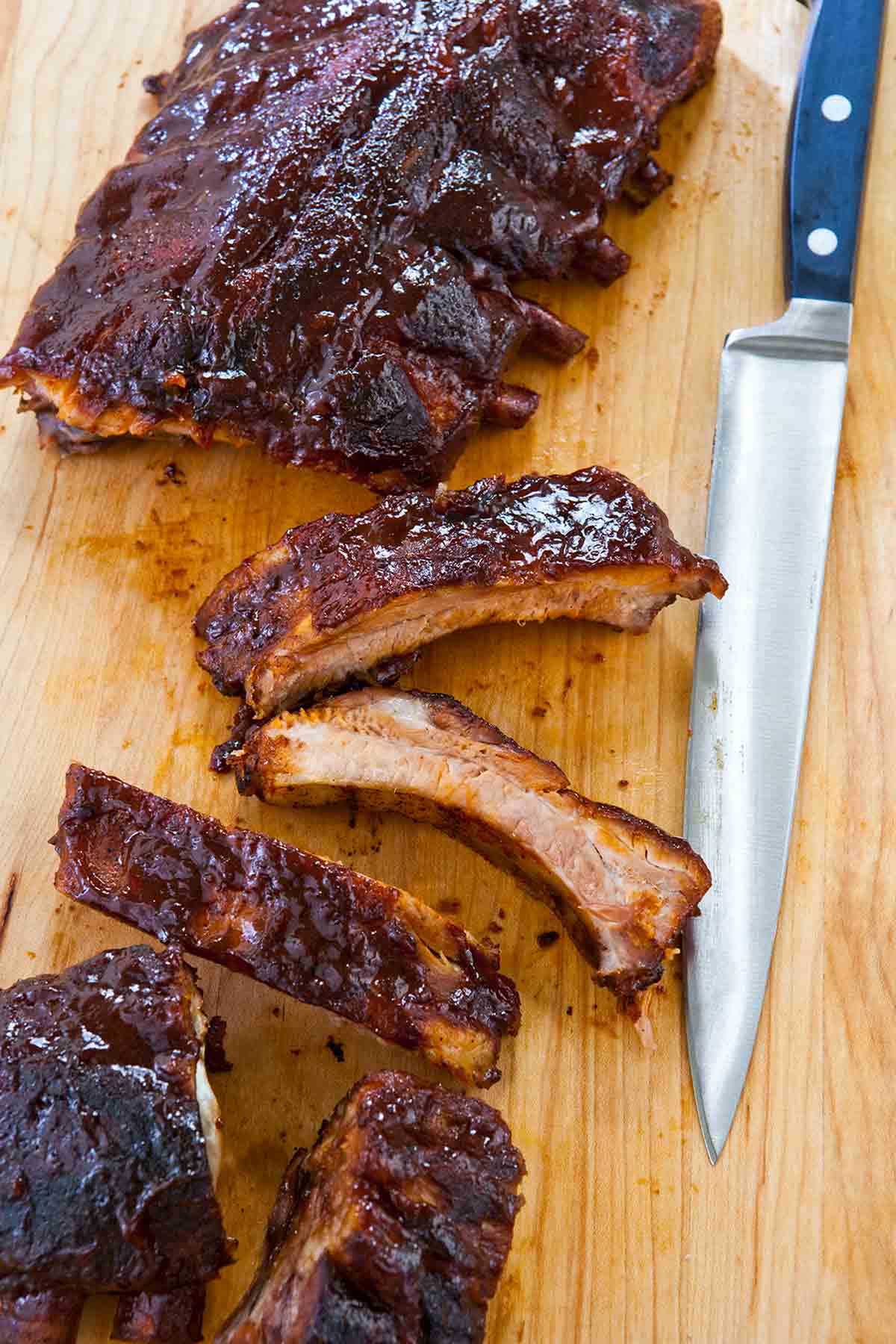 A rack of slow cooker ribs on a cutting board with four single ribs cut off.