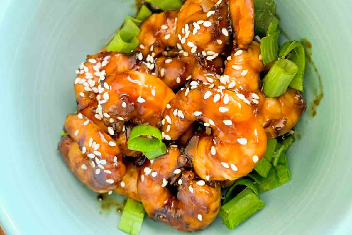 A bowl of glazed shrimp topped with sliced scallions and sesame seeds.