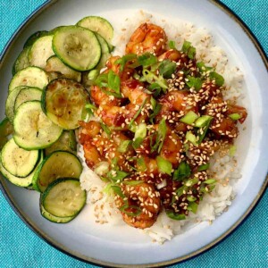 A plate of honey garlic shrimp on a bed of rice, with roasted zucchini slices on the side.