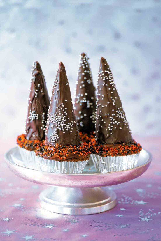 Four cupcakes with chocolate icing, topped with chocolate wizard hats.