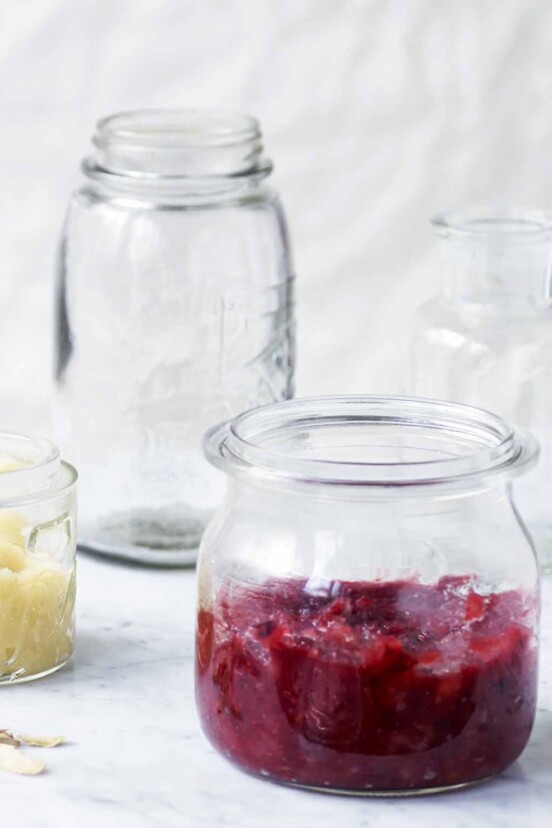 A glass jar half filled with apple cranberry sauce, with a second jar of applesauce in the background.