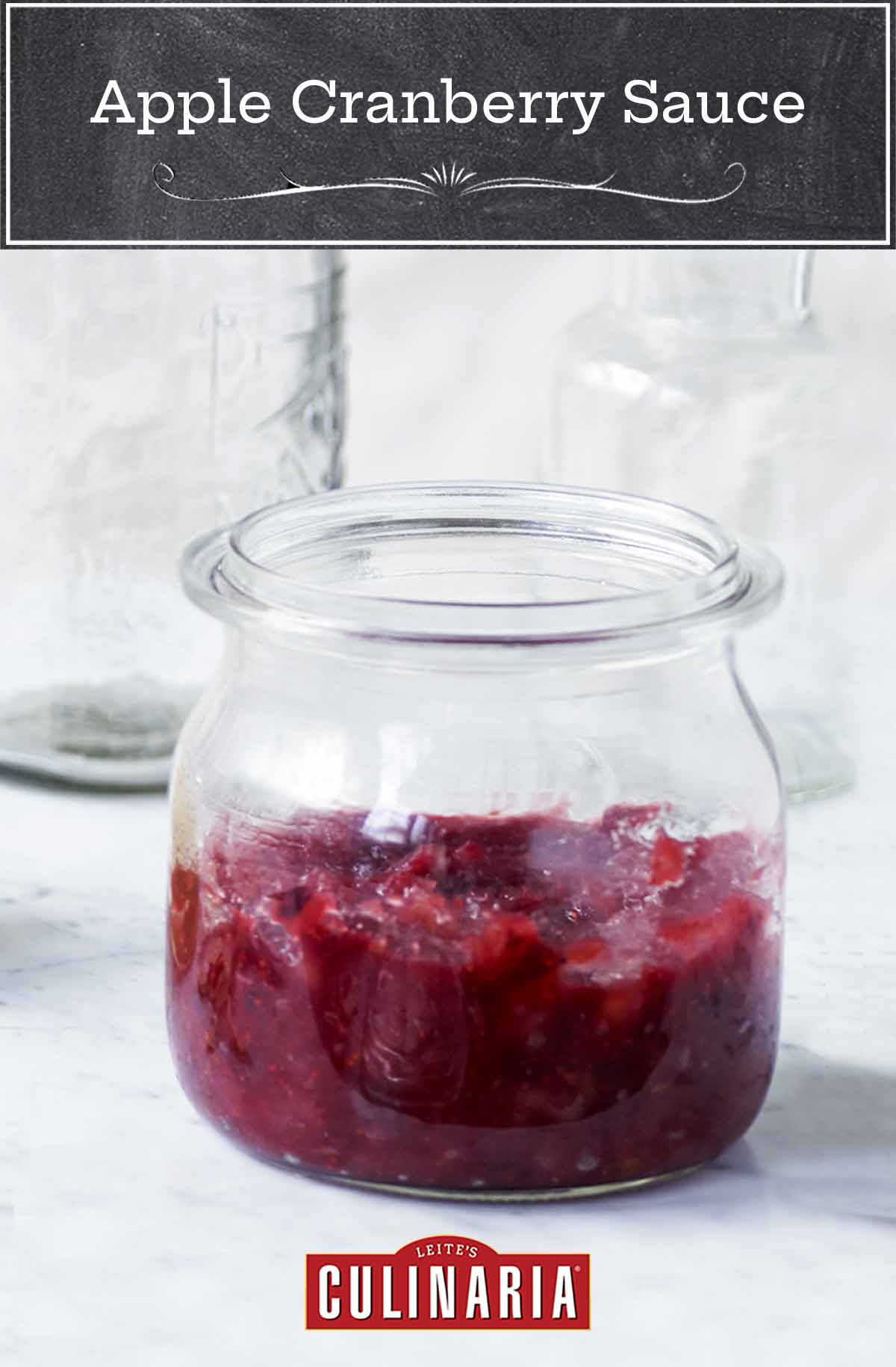 A glass jar half filled with apple cranberry sauce, with a second jar of applesauce in the background.