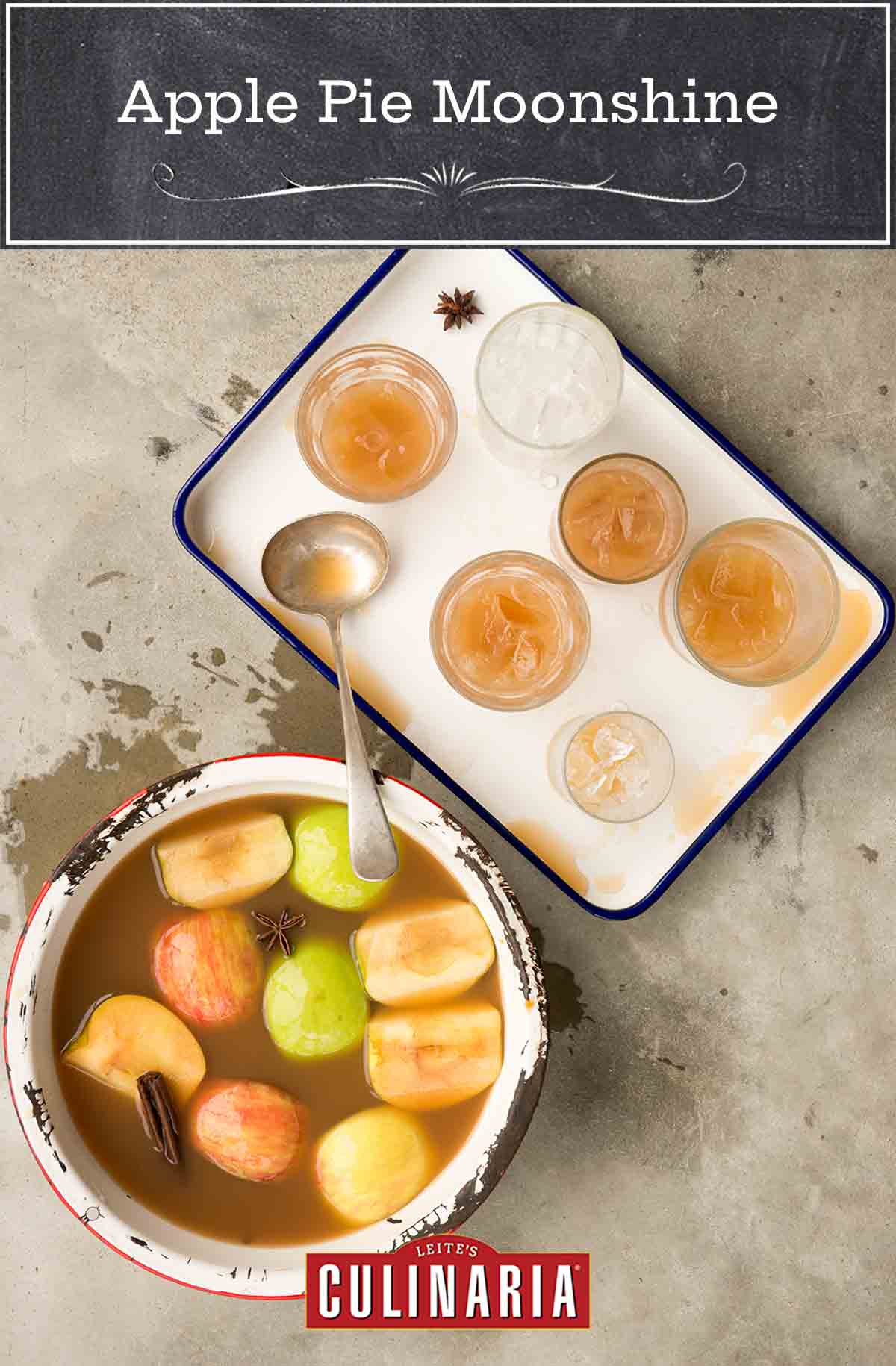A chipped pot filled with apple pie moonshine, apple wedges and whole spices with a tray of glasses filled with the moonshine beside it.