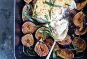 A rectangular baking dish with a block of cooked feta in the center, surrounded by halved figs and tarragon leaves.