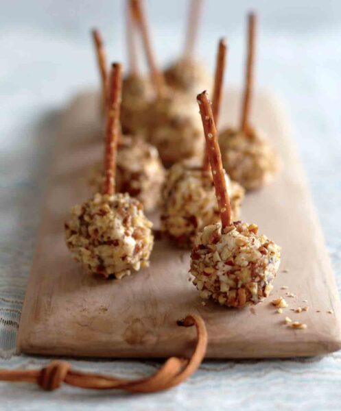 Golf-ball size cheese balls with pretzel stems sitting on a wooden cheese board.