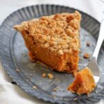 A wedge of bourbon sweet potato pie topped with a crumbly brown sugar streusel on a metal plate.