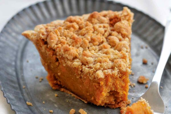 A wedge of bourbon sweet potato pie topped with a crumbly brown sugar streusel on a metal plate.
