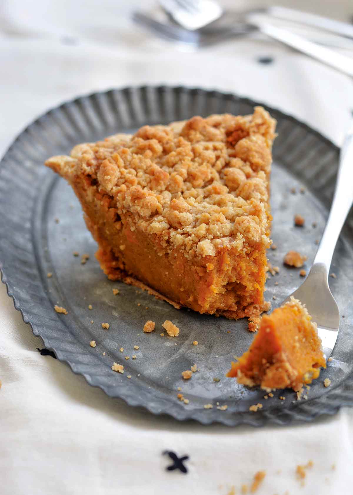 A wedge of bourbon sweet potato pie topped with a crumbly brown sugar streusel on a metal plate.