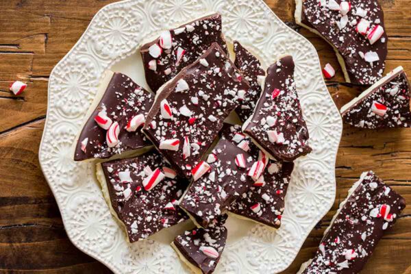 A decorative white plate filled with irregular pieces of candy cane bark.