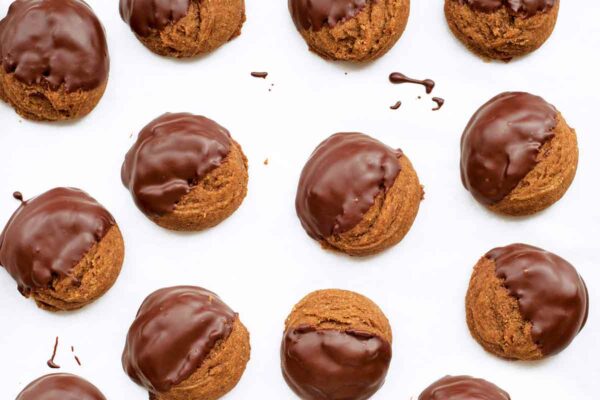 A dozen mounded molasses cookies, half of each is covered in chocolate on a white background.