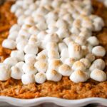 A white dish filled with sweet potato casserole, topped with toasted marshmallows.