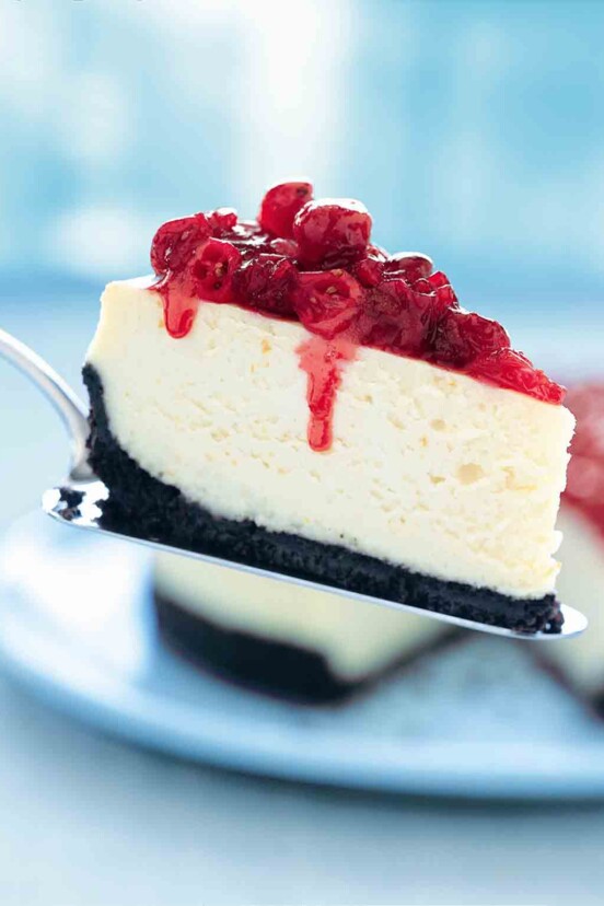 A slice of cheesecake topped with cranberries on a silver cake lifter.